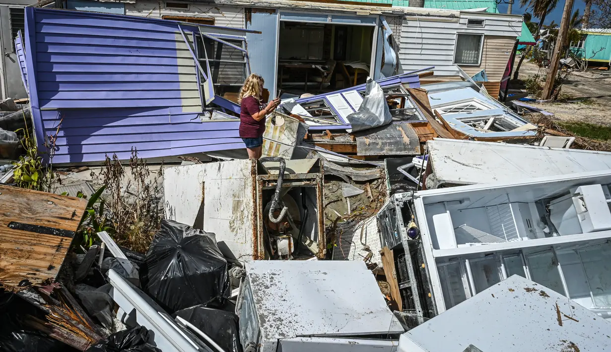 Seorang wanita berjalan melewati puing-puing rumah yang hancur di Pulau Matlacha di Lee County Florida pada 7 November 2022. Badai subtropis Nicole yang langka dapat menghantam pantai timur Florida minggu ini ketika penduduk berusaha pulih dari Badai Ian yang mematikan. (AFP/ Giorgio Viera)