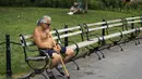 Seorang pria tanpa mengenakan baju beristirahat saat siang hari yang panas di Washington Square Park di New York City (17/7/2019). Panas terik bergerak ke daerah Kota New York, dengan suhu yang diperkirakan akan mencapai 100 derajat pada akhir pekan ini.  (AFP Photo/Drew Angerer)