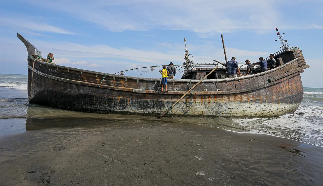 Penduduk desa melihat perahu kayu yang digunakan oleh orang-orang Rohingya di Pidie, provinsi Aceh pada 27 Desember 2022. Pengungsi Rohingya menerima perawatan medis darurat setelah sebuah kapal yang membawa hampir 200 orang mendarat di Indonesia pada 26 Desember, kata pihak berwenang, dalam pendaratan keempat di negara dalam beberapa bulan terakhir. (AFP/Amanda Jufrian)