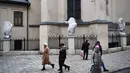 Pejalan kaki berjalan melewati patung-patung yang dibungkus dengan plastik di Katedral Latin di Lviv, 5 Maret 2022. Warga kota Lviv membungkus semua patung yang ada di kota tersebut untuk melindungi warisan sejarahnya dari kerusakan akibat serangan di tengah konflik Rusia-Ukraina. (Daniel LEAL/AFP)