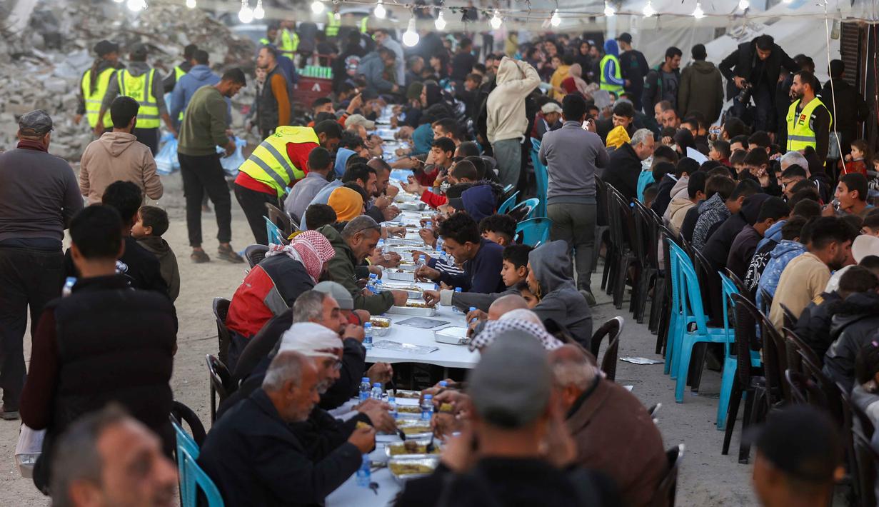 Antusiasme menyambut Ramadan tetap terasa di tengah kondisi sebagian besar warga yang telah kehilangan orang terkasih akibat perang berkepanjangan antara Israel dan Hamas di hampir seluruh wilayah Gaza. Tampak dalam foto, warga Palestina berkumpul untuk berbuka puasa bersama yang diselenggarakan oleh Yayasan IHH Turki, di tengah reruntuhan bangunan yang hancur di Kota Gaza pada Rabu 18 Februari 2026. (Omar AL-QATTAA/AFP)