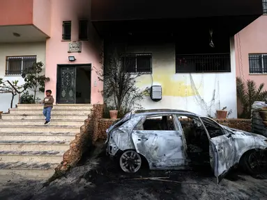 Seorang anak Palestina berdiri di sisi mobil yang hancur dan di luar rumah yang terbakar setelah serangan yang dilaporkan dilakukan oleh pemukim Israel di desa Deir al-Hatab, sebelah timur kota Nablus, di Tepi Barat, wilayah yang diduduki Israel pada Senin 23 Maret 2026. Penyerangan yang dilakukan pemukim ilegal Israel di Tepi Barat terhadap warga Palestina kembali terjadi. (JAAFAR ASHTIYEH/AFP)