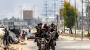 Para pria berkendara bersama di belakang gerobak roda tiga di sepanjang jalan Salaheddin, Deir el-Balah, Jalur Gaza tengah pada 21 Juli 2025, sementara di belakangnya mengepul asap akibat pemboman Israel. (Eyad BABA/AFP)