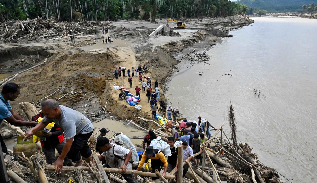 Kondisi ini memaksa warga mencari jalan seadanya untuk menyeberang sungai dengan aman. Tampak dalam foto, warga menyeberangi sungai di jembatan yang baru dibangun yang menghubungkan Aceh dan Provinsi Sumatera Utara setelah hancur akibat banjir bandang di Sungai Peusangan, Distrik Bireuen, Provinsi Aceh, Selasa 9 Desember 2025. (CHAIDEER MAHYUDDIN/AFP)