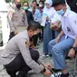 Kapolres Garut AKBP Wirdhanto Hadicaksono terpaksa bertekuk lutut membetulkan tali sepatu milik pelajar disela-sela pemberian sepatu korban banjir bandang Garut di kantor desa Jayaraga. (Liputan6.com/ Jayadi Supriadin)