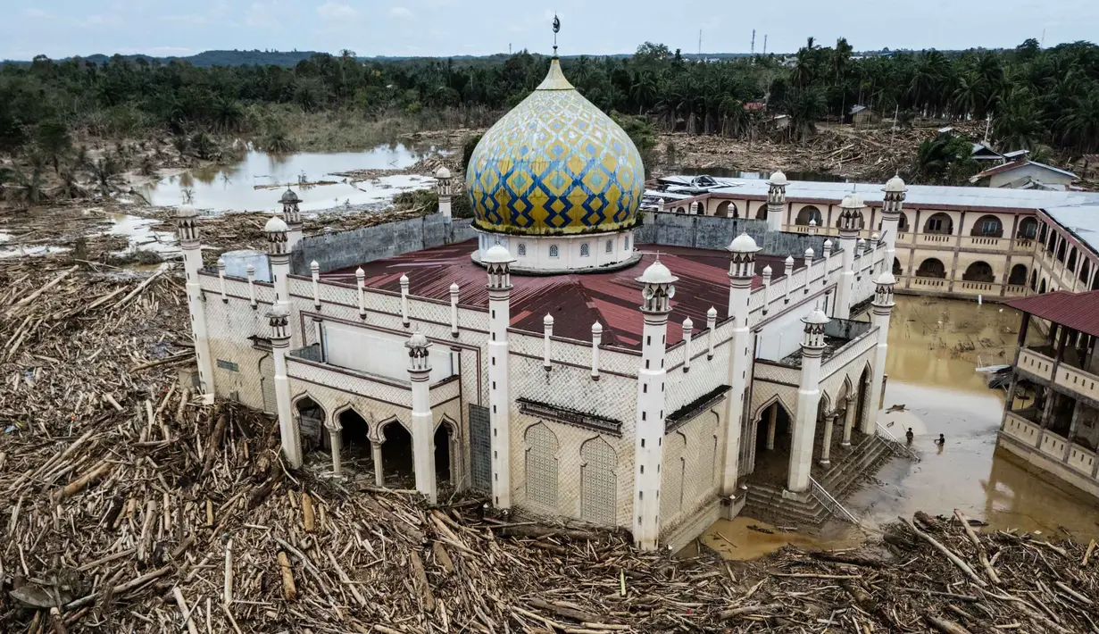 Jejak bekas lumpur dan air banjir pun masih terlihat di dinding dekat atap lantai dua bangunan. Tampak foto udara menunjukkan tumpukan pohon tumbang yang tersapu banjir bandang sekitar tiga minggu lalu di Pesantren Darul Mukhlisin dan masjid yang terhubung dengan pesantren tersebut di Aceh Tamiang, pada Minggu 14 Desember 2025. (Foto oleh AFP)