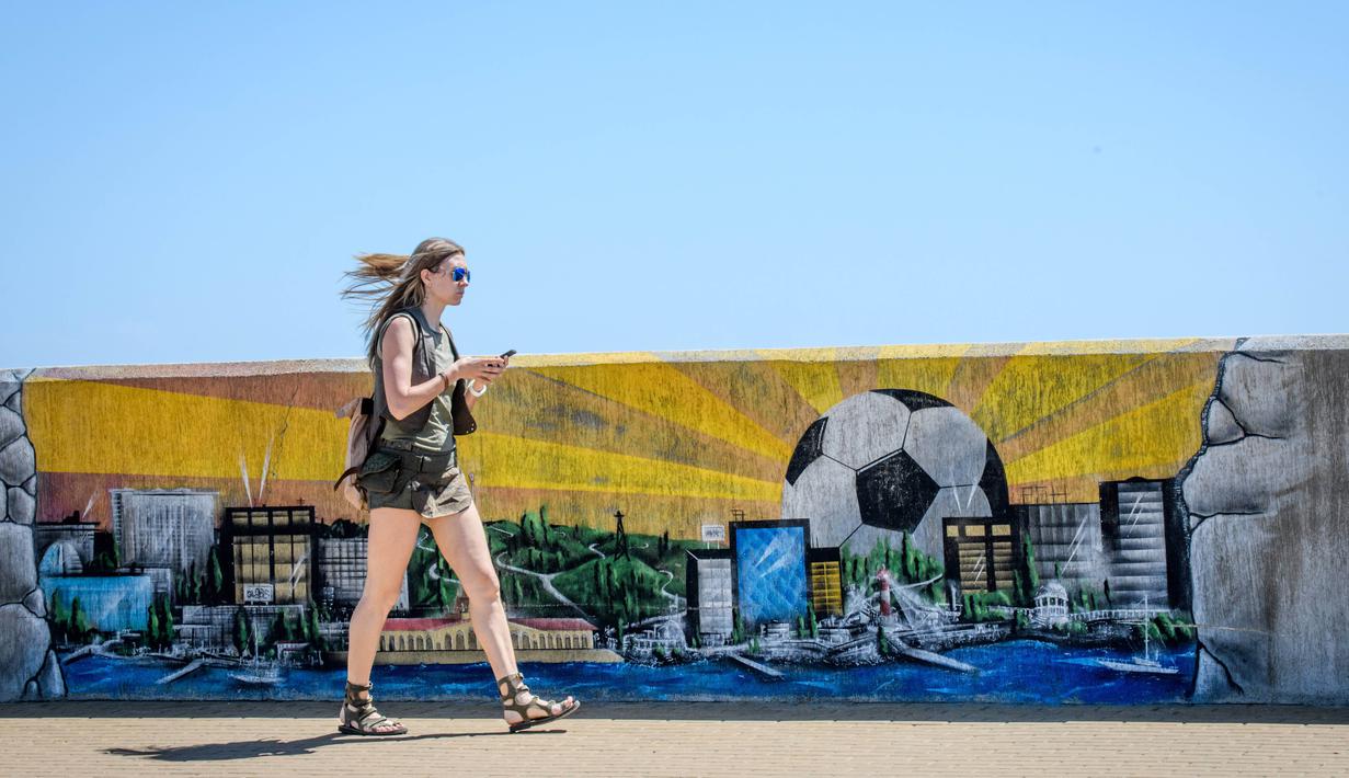 Seorang wanita melintas dekat mural seputar Fisht Olympic Stadium di Sochi, Rusia, (17/5/2018). Stadion tersebut akan menjadi saksi laga perdana Portugal melawan Spanyol. (AFP/Mladen Antonov)