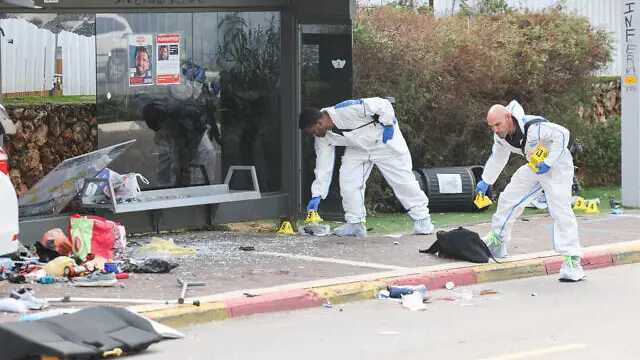 Personel darurat dan keamanan Israel berdiri di samping mobil yang rusak usai serangan teroris di pusat Kota Raanana, pada 15 Januari 2024. (Jack Guez / AFP)