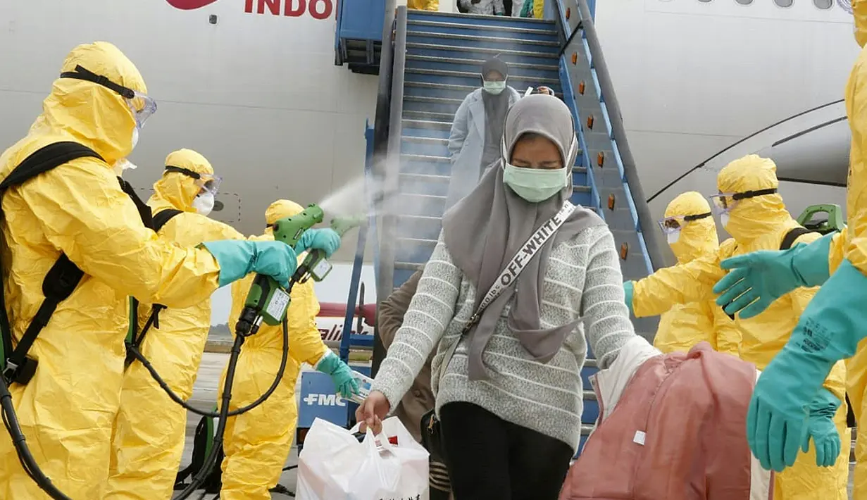 Petugas menyemprotkan cairan disinfektan ke WNI yang dievakuasi dari Wuhan, China saat tiba di bandara internasional Hang Nadim, Batam, Minggu (2/2/2020). Para WNI langsung ke luar pesawat untuk selanjutnya menuju Natuna, Kepulauan Riau. (Photo by Handout/Indonesian Embassy/AFP)