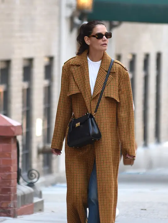 Katie Holmes memiliki banyak tas selempang, seperti tas Louis Vuitton LV Arch ini. Ia melengkapi tampilannya dengan mantel kotak-kotak dan stiletto dari Jimmy Choo. Foto: Vogue.