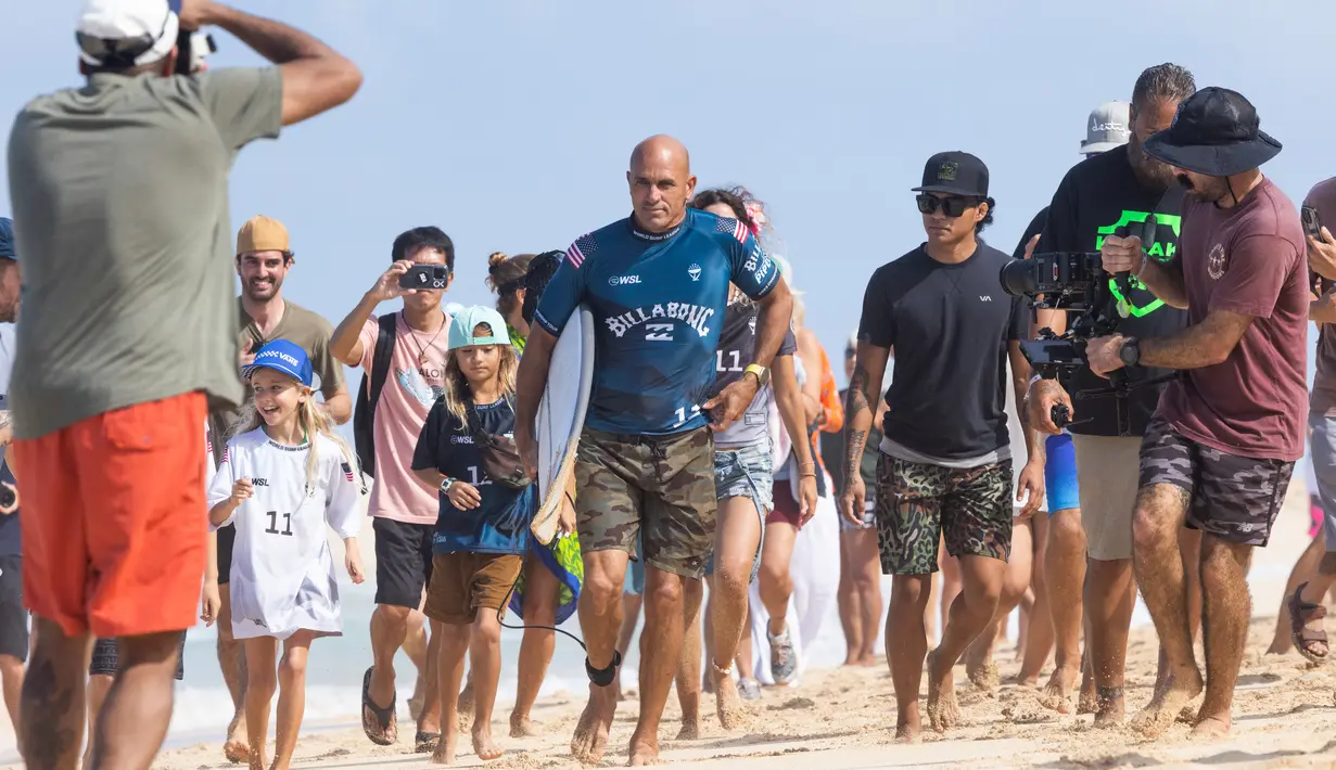 Peselancar AS Kelly Slater dikelilingi oleh para penggemar saat dia berjalan ke air pada hari pertama Billabong Pipeline Pro di Banzai Pipeline di pantai utara Oahu, Hawaii, pada 1 Februari 2023. Kejuaraan ini berlangsung dari 29 Januari hingga 10 Februari 2023. (AFP/Brian Bielmann)
