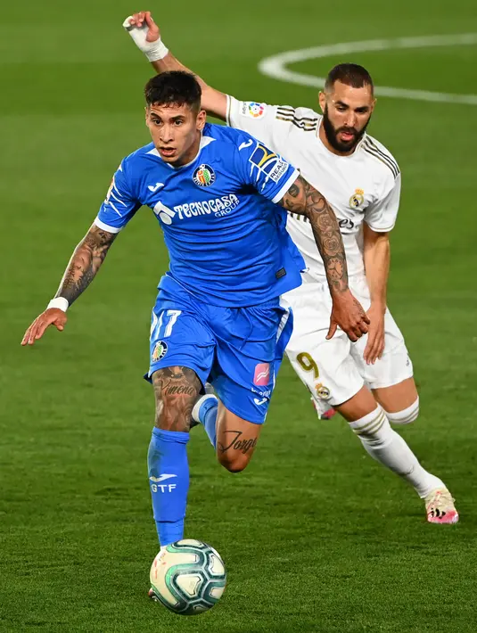 Bek Getafe, Mathias Olivera membawa bola dari kejaran penyerang Real Madrid, Karim Benzema pada pertandingan lanjutan La Liga Spanyol di stadion Alfredo di Stefano di Valdebebas, Madrid (2/7/2020). Madrid menang tipis atas Getafe 1-0.  (AFP Photo/Gabriel Bouys)
