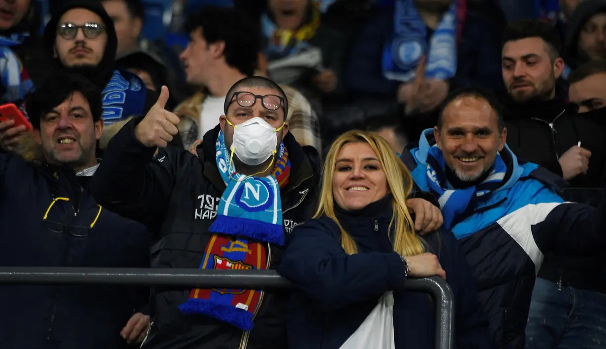 Seorang suporter Napoli mengenakan masker menunggu dimulainya pertandingan antara Napoli dan Barcelona di Stadion San Paolo di Naples, Italia, Selasa, (25/2/2020). Italia melaporkan kenaikan kasus infeksi virus Corona COVID- 91 menjadi lebih 272 kasus. (AFP Photo/Filippo Monteforte)