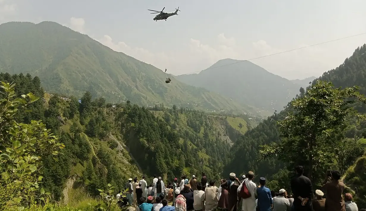 Orang-orang menyaksikan seorang tentara terjun dari helikopter selama misi penyelamatan untuk menyelamatkan para siswa yang terjebak di keeta gantung di desa Pashto di provinsi pegunungan Khyber Pakhtunkhwa, pada 22 Agustus 2023. (AFP)