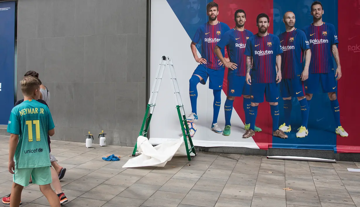 Seorang anak mengenakan jersey Neymar melewati sebuah poster baru yang dipasang di luar Stadion Camp Nou di Barcelona (2/8). Sebelumnya, poster tersebut menampilkan pemain depan Barcelona Neymar dari Brasil. (AFP Photo/Josep Lago)