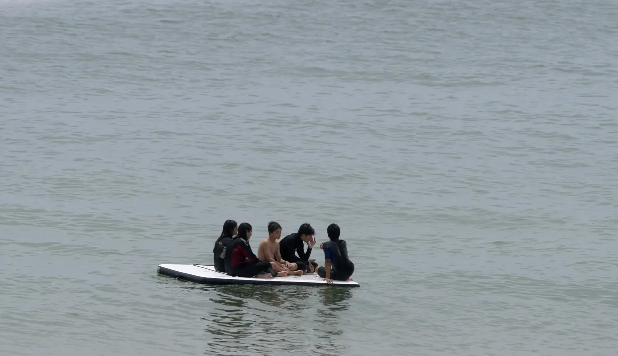 Anak-anak duduk di atas rakit di laut yang tenang di Pantai Carcavelos, di luar Lisbon, Selasa (12/7/2022). Portugal mengalami gelombang panas yang membuat pemerintah mengumumkan keadaan siaga mulai Senin hingga Jumat karena meningkatnya risiko kebakaran hutan. (AP Photo/Armando Franca)