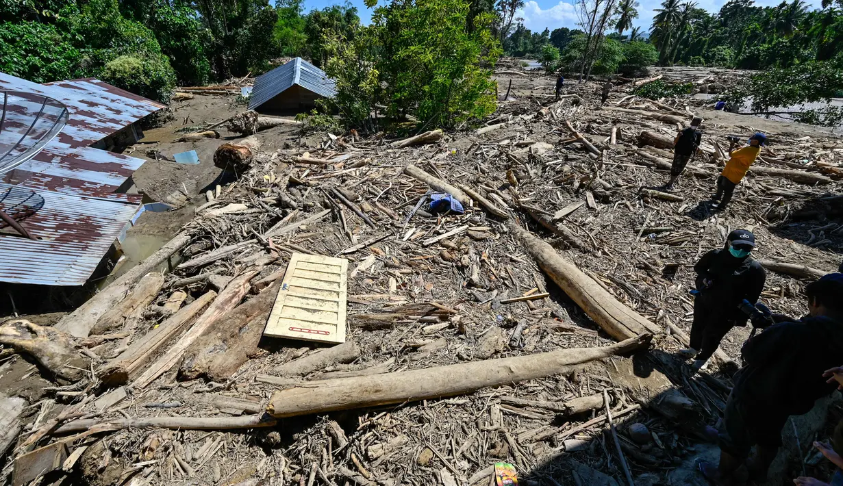 Hingga saat ini, daerah terdampak banjir bandang di Meureudu, Kabupaten Pidie Jaya, masih dipenuhi oleh lumpur tebal, pasir, dan puing-puing material bangunan serta kayu gelondongan. Tampak dalam foto, orang-orang berjalan melintasi lumpur dan puing-puing di daerah terdampak banjir di Meureudu, Kabupaten Pidie Jaya, Provinsi Aceh, pada 30 November 2025. (CHAIDEER MAHYUDDIN/AFP)