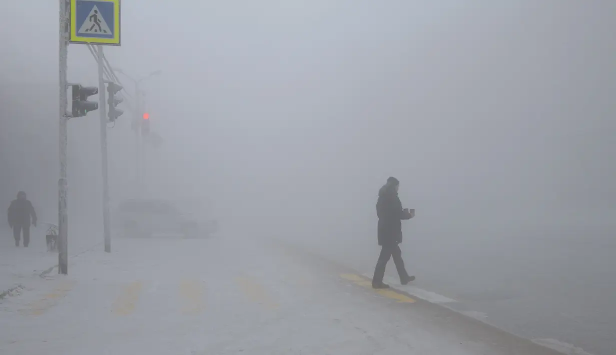 Seorang pria membawa kopi panas menyeberang jalan saat suhu turun hingga sekitar -50 derajat (-58 derajat Fahrenheit) di Yakutsk, Rusia pada Rusia, Sabtu (16/1/2021).  Yakutsk atau Yakutia tersohor sebagai kota terdingin di dunia. (AP Photo/Tatiana Gasich)