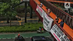 Sejumlah aktivis yang tergabung dalam Extintion Rebellion (XR) dan Walhi Jakarta melakukan aksi di JPO Pinisi, Jalan Jenderal Sudirman, Jakarta, Senin (14/11/2022). Aksi tersebut dilakukan untuk menyerukan kepada para pemimpin agar menghentikan “pencucian hijau” dan praktik ekonomi “business-as-usual” yang secara sistematis memperburuk krisis iklim dan mendorong umat manusia pada kehancuran ekologis & kepunahan massal. Negara-negara G20 turut menyumbang atas 80 persen emisi karbon dunia dan 60 persen populasi penduduk bumi. (Liputan6.com/Angga Yuniar)