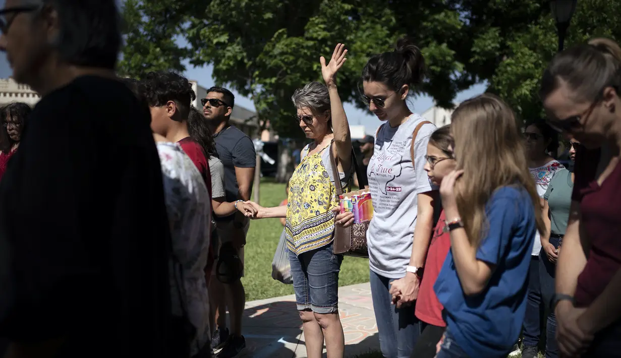 Orang-orang berkumpul dengan kepala tertunduk sementara beberapa berdoa di tempat peringatan bagi para korban, termasuk sepupunya, yang tewas dalam penembakan di Robb Elementary School, Uvalde, Texas, Amerika Serikat, 28 Mei 2022. (AP Photo/Wong Maye-E)