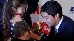 Penyerang Barcelona, Luis Suarez menunjukan sepatu emas 2016 kepada kedua anaknya di Barcelona, Spanyol (20/10). Suarez mengalahkan rivalnya, seperti Gonzalo Higuain, Cristiano Ronaldo, dan Zlatan Ibrahimovic. (REUTERS/Albert Gea)