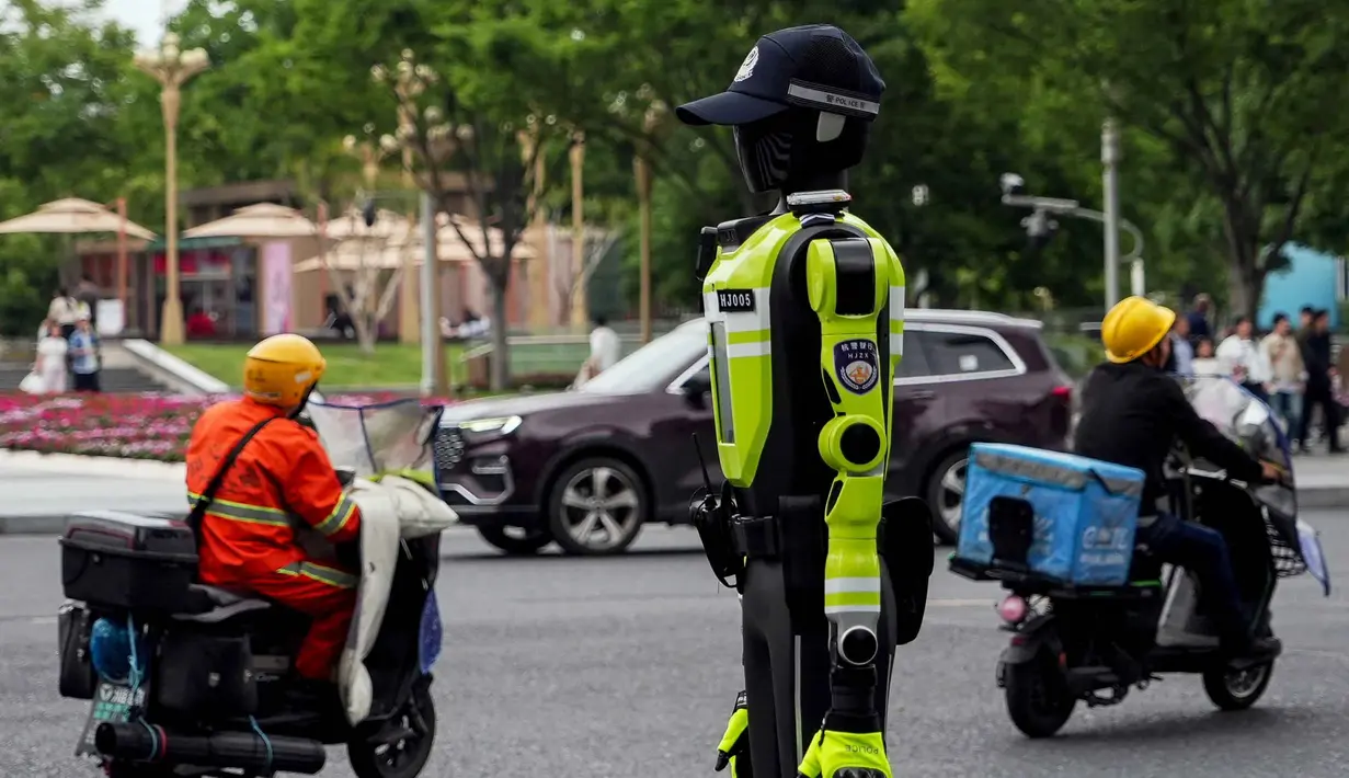 Robot-robot humanoid ini ditempatkan di persimpangan jalan utama dan area strategis, termasuk di sekitar kawasan wisata. Tampak dalam foto, orang-orang berkendara melewati robot polisi humanoid di Hangzhou, provinsi Zhejiang Timur, Tiongkok pada Minggu 3 Mei 2026. (Agatha CANTRILL/AFP)