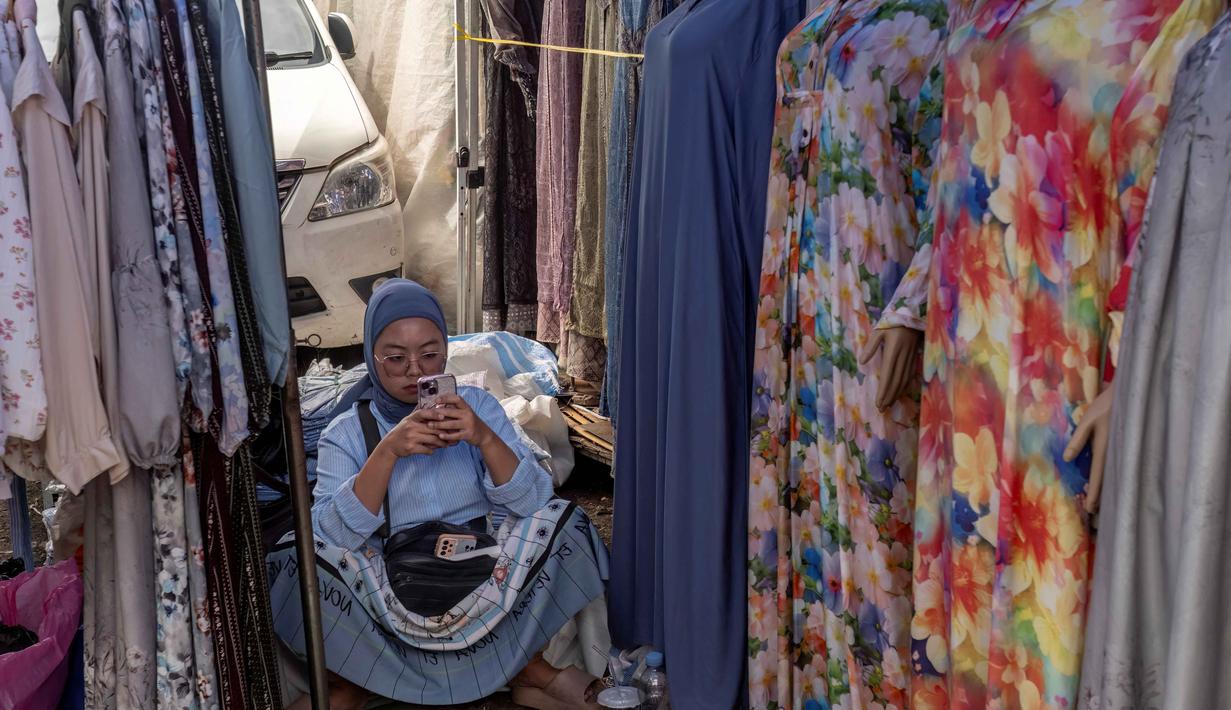 Pembersihan pasar dari pakaian bekas impor akan langsung membuka peluang bagi lini usaha lokal yang selama ini terhimpit. Tampak dalam foto, seorang penjual menggunakan telepon selulernya sambil menunggu pelanggan di sebuah kios pakaian di salah satu pasar tradisional, Jakarta, Kamis 20 November 2025. (BAY ISMOYO/AFP)