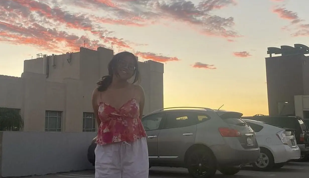 Dengan gaya rambut diikat, Cinta tampil mengenakan atasan spaghetti strap merah bermotif dipadukan celana putih panjangnya. [@cintakuya]