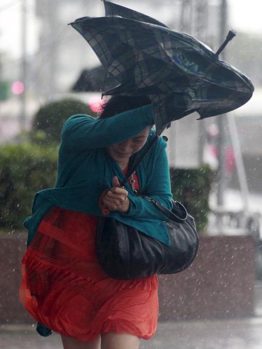 Warga berlindung di balik payung untuk menghindari angin kencang yang disebabkan topan Dujuan di Taipei, Taiwan, Senin (28/9). Ribuan orang diungsikan untuk menghadapi topan raksasa Dujuan yang diprediksikan akan menyerang Taiwan. (REUTERS/Pichi Chuang)