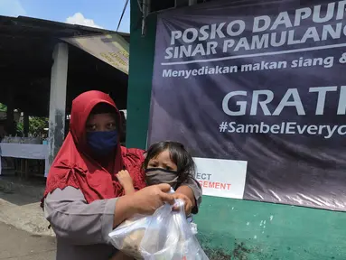 Seorang ibu menggendong anaknya sambil membawa nasi bungkus yang disediakan gratis di Kompleks Sinar Pamulang Permai, Pamulang Barat, Tangerang Selatan, Senin (13/4/2020).  (merdeka.com/Arie Basuki)