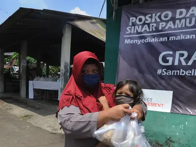 Seorang ibu menggendong anaknya sambil membawa nasi bungkus yang disediakan gratis di Kompleks Sinar Pamulang Permai, Pamulang Barat, Tangerang Selatan, Senin (13/4/2020).  (merdeka.com/Arie Basuki)