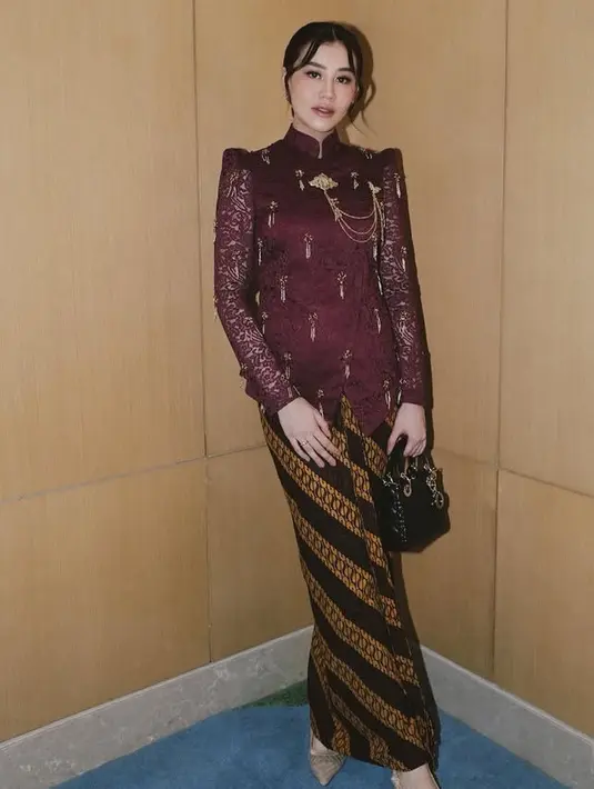 Untuk akad nikah, ia mengenakan kebaya brokat warna maroon dengan model janggan yang memiliki ciri khas kerah tinggi. Kebaya yang dihiasi beads rumbai dipadukan bros rantai warna gold serta bawahan kain batik. Ia juga membawa mini bag lady Dior hitam. [@aaliyahmassaid]