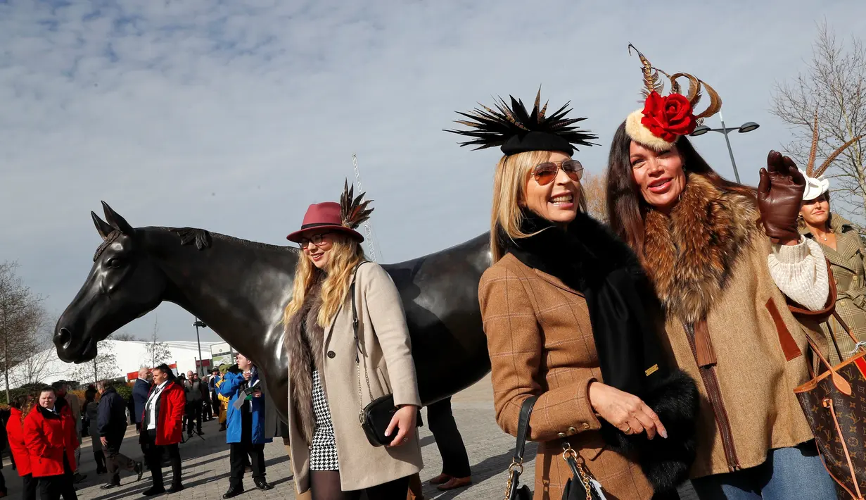 Dua wanita berpose di samping patung "Best Mate" saat orang-orang tiba pada hari pertama Festival Cheltenham di Cheltenham Racecourse, di Cheltenham, Inggris (15/3/2022). Kehadiran para wanita memberikan nuansa tersendiri di kompetisi pacuan kuda tersebut. (Mike Egerton/PA via AP)