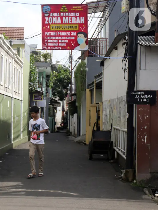 Warga melintasi spanduk zona merah kawasan RW 01 Kelurahan kalibata, Jakarta, Selasa (9/2/2021). Pemerintah mulai menerapkan PPKM skala mikro mulai 9-22 Februari 2021 untuk 7 provinsi yakni DKI Jakarta, Jawa Barat, Banten, Jawa Tengah, Yogyakarta, Jawa Timur, dan Bali. (Liputan6.com/Herman Zakharia)