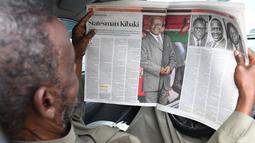 Seorang pria membaca koran lokal dengan penghormatan untuk mantan presiden Kenya Mwai Kibaki, di Nairobi, pada 23 April 2022. Mantan Presiden Kenya, Mwai Kibaki, yang pernah memimpin negara Afrika Timur itu selama lebih dari satu dekade, dikabarkan meninggal dunia pada Jumat (22/4) di usia 90 tahun. (Simon MAINA / AFP)