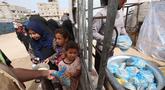 Seorang anak pengungsi Palestina mengambil sebungkus roti sementara yang lain menunggu giliran mereka dari salah satu dapur amal di kamp pengungsi Bureij, Jalur Gaza Tengah pada Senin 18 Mei 2026. (Eyad Baba/AFP)