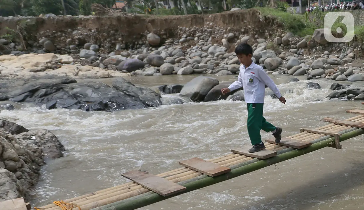 Siswa melintasi jembatan darurat berbahan bambu di Kampung Ciasahan, Desa Sukamaju, Kabupaten Bogor, Kamis (6/2/2020). Pembangunan kembali jembatan Ciasahan yang ambruk akibat banjir bandang pada Rabu (1/1) itu diharapkan mampu memulihkan aktivitas dan perekonomian warga. (merdeka.com/Arie Basuki)