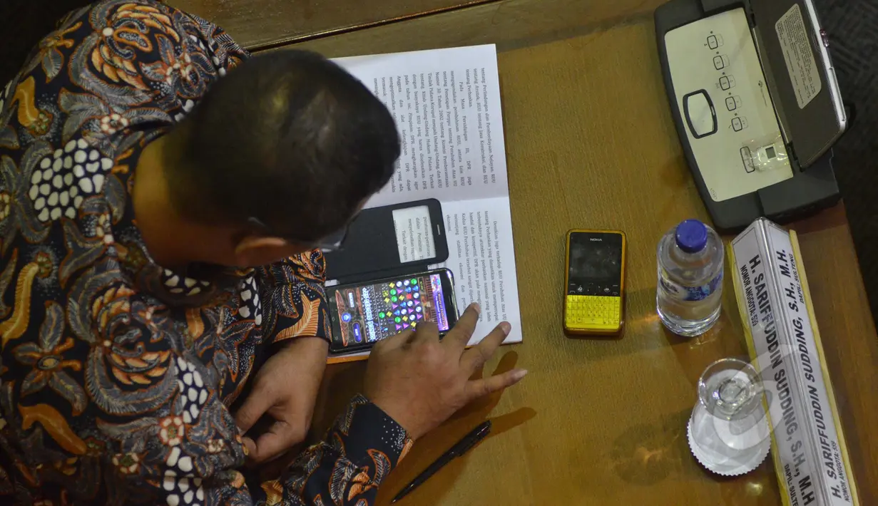 Salah satu anggota dewan terlihat asyik memainkan game di ponselnya saat menghadiri sidang paripurna pembukaan reses, Jakarta, Senin (23/3/2015). Sekitar 255 anggota dewan tak hadir dalam sidang pembukaan reses tersebut. (Liputan6.com/Faisal R Syam)