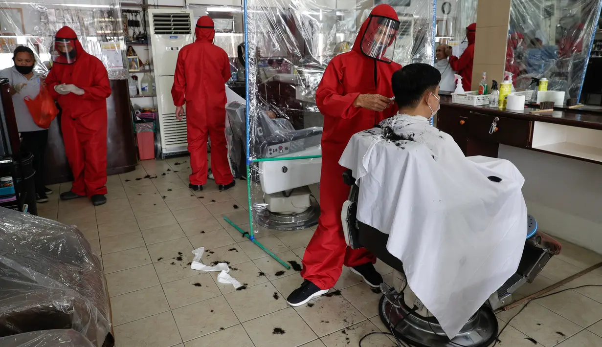 Tukang cukur mengenakan alat pelindung diri (APD) saat memotong rambut pelanggan di sebuah tempat pangkas rambut di Manila, 8 Juni 2020. Filipina mengizinkan barbershop dan salon kecantikan beroperasi kembali dengan menerapkan langkah-langkah ketat pencegahan pandemi Covid-19. (AP/Aaron Favila)