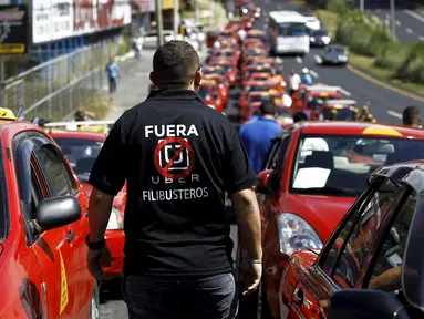Seorang sopir taksi mengenakan kaos bertuliskan "Uber, keluar dari Kosta Rika" saat menggelar unjuk rasa di San Jose, Senin (1/2).  Mereka melakukan protes terhadap taksi Uber yang mulai beroperasi di Kosta Rika. (REUTERS/Juan Carlos Ulate)