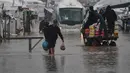 Situasi ini memperburuk genangan air di dalam dan sekitar tenda. Tampak dalam foto, warga Palestina berjalan melintasi jalan yang tergenang banjir setelah hujan lebat di Khan Younis, Jalur Gaza selatan, Kamis 11 Desember 2025. (AP Photo/Abdel Kareem Hana)