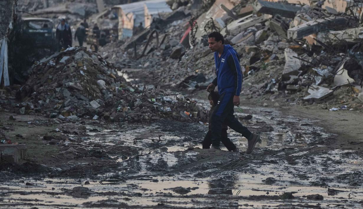 Warga Palestina berjalan di tengah bangunan yang hancur akibat serangan udara dan darat Israel di Kota Gaza, Selasa 6 Januari 2026. Komite Internasional Palang Merah (ICRC) terus berupaya menyalurkan bantuan ke Gaza. (AP Photo/Jehad Alshrafi)