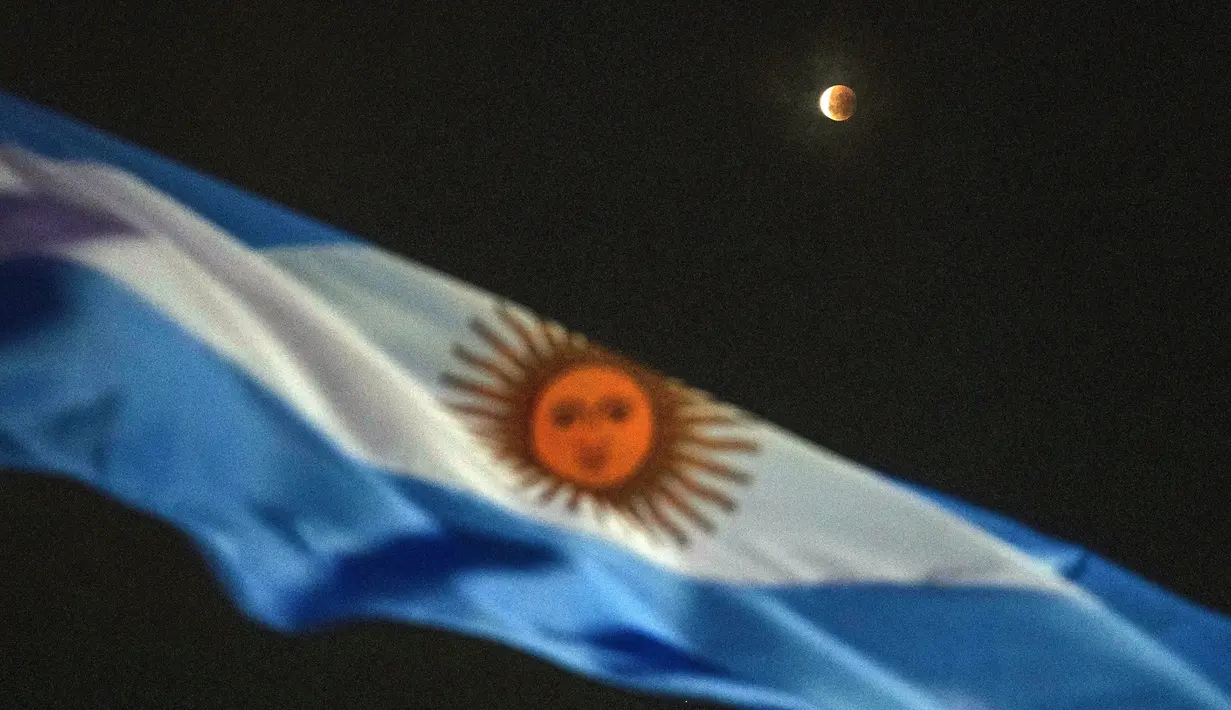Gerhana bulan terlihat di belakang bendera Argentina saat blood moon pertama tahun ini di Buenos Aires, Argentina, Senin (16/5/2022). (AP Photo/Rodrigo Abd)