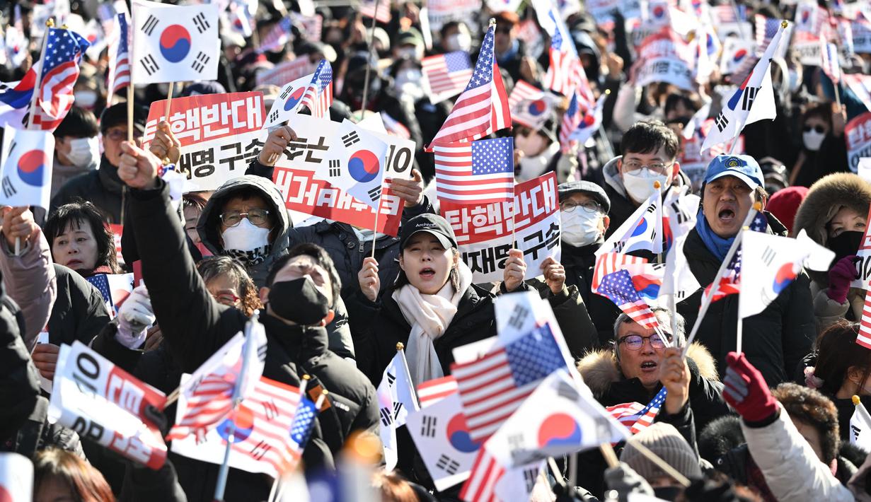 Para pendukung Presiden Korea Selatan yang dimakzulkan, Yoon Suk Yeol, melambaikan bendera Amerika Serikat dan Korea Selatan saat mereka berkumpul di dekat kediaman kepresidenan di Seoul pada tanggal 31 Desember 2024. (JUNG YEON-JE/AFP)