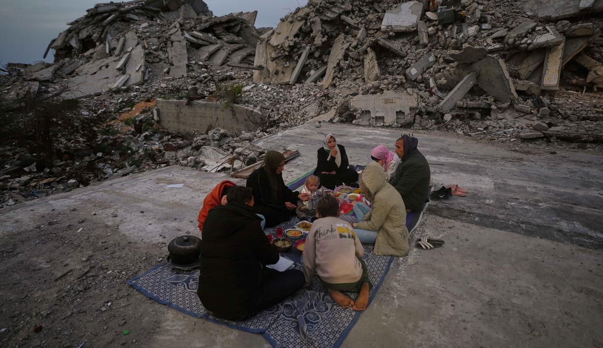 Meski krisis kemanusiaan terus membayangi kehidupan mereka di Jalur Gaza, tradisi Ramadan dengan berbagi makanan sederhana saat berbuka puasa tetap terjaga kokoh. Tampak dalam foto, anggota keluarga Al-Najar berbuka puasa selama bulan suci Ramadan di tengah reruntuhan bangunan yang hancur di Kota Gaza, Jumat 13 Maret 2026. (AP Photo/Jehad Alshrafi)