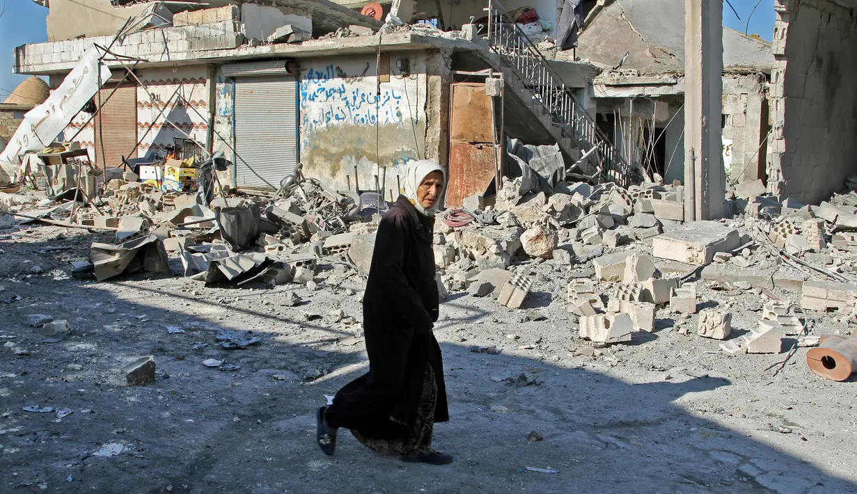 Seorang wanita berjalan melewati lokasi pemboman pemerintah Suriah di Desa Maasaran, Distrik Maaret al-Numan, Provinsi Idlib, Selasa (17/12/2019). Ribuan warga Maaret al-Numan telah melarikan diri dalam beberapa hari terakhir di tengah serangan udara dan penembakan yang intens. (Abdulaziz KETAZ/AFP)