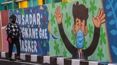Seorang perempuan melewati mural yang mengajak orang untuk memakai masker di tengah pandemi Covid-19 di Surabaya, Minggu (25/10/2020). Mural di sepanjang dinding itu sebagai sarana imbauan kepada masyarakat untuk menerapkan protokol kesehatan pencegahan penularan COVID-19. (Juni Kriswanto/AFP)
