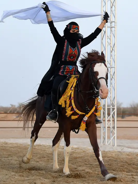 Perempuan Arab mengibarkan kain putih saat menunggangi kuda dalam Festival Souk Okaz 2019 di Kota Taif, Arab Saudi, Rabu (7/8/2019). Tahun ini merupakan pertama kalinya perempuan diizinkan untuk berpartisipasi dalam Festival Souq Okaz 2019. (AMER HILABI/AFP)