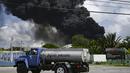 Asap hitam dari kebakaran besar di depot bahan bakar terlihat saat sebuah truk air melewati jalan di Matanzas, Kuba (7/8/2022). Kuba meminta bantuan Sabtu (7/7) untuk mengatasi kebakaran besar yang menyebabkan 77 orang terluka dan 17 petugas pemadam kebakaran hilang. Sekitar 800 orang telah dievakuasi dari daerah tersebut. (AFP/Yamil Lage)