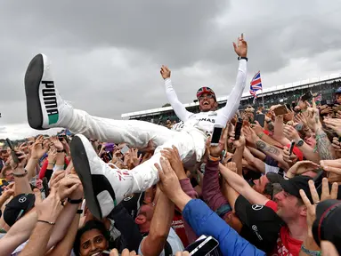 Pembalap Mercedes Lewis Hamilton melakukan selebrasi bersama penggemarnya usai berhasil memenangkan GP Inggris di sirkuit Silverstone, (16/7).  Hamilton berhasil menjuarai GP Inggris untuk kali keempat secara beruntun. (AFP Photo/Andrej Isakovic)